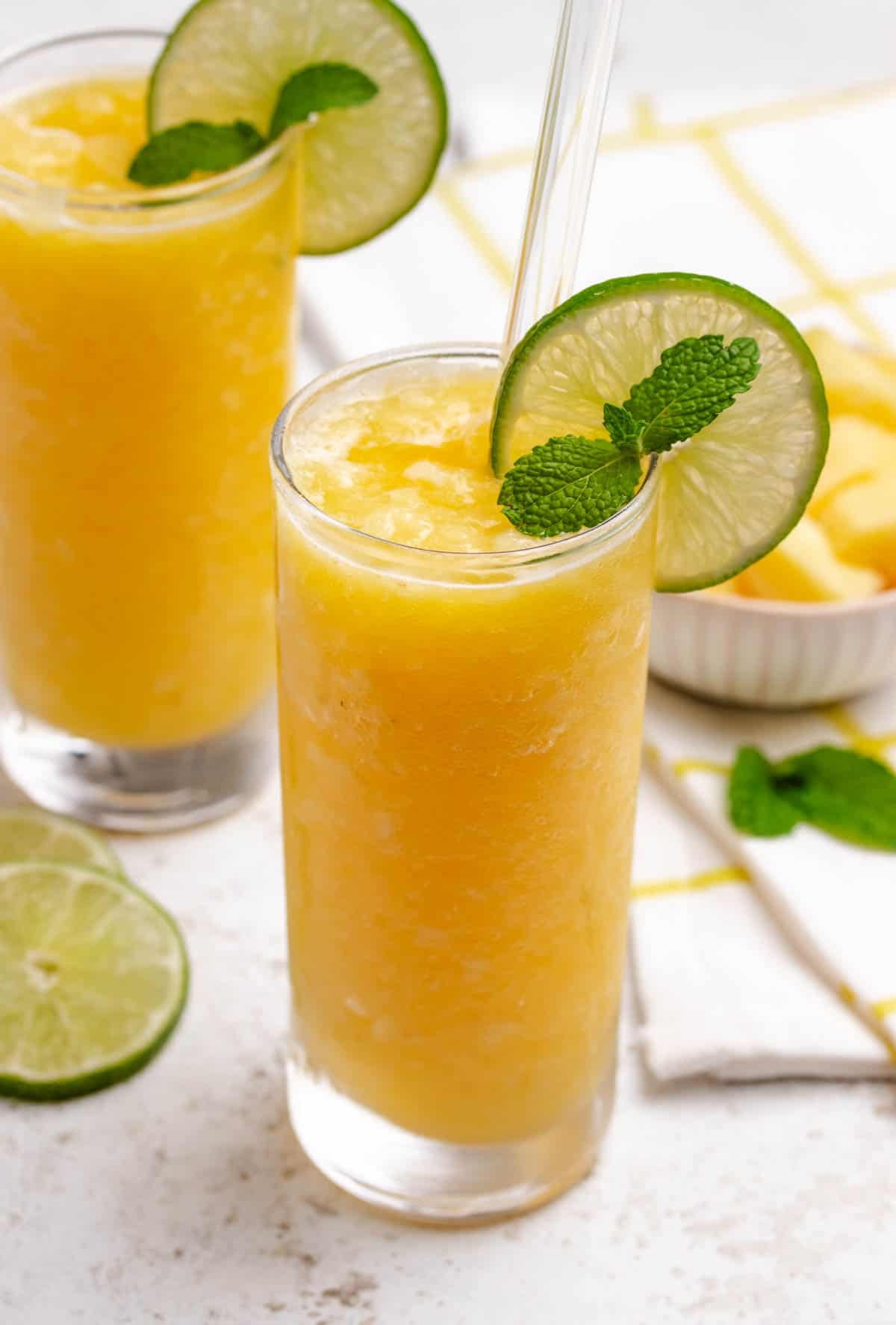 Pineapple slush in a glass with a lime wheel, mint, and a straw.