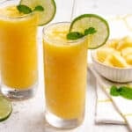 Pineapple slushie in a glass with a lime wheel, sprig of mint, and a straw.
