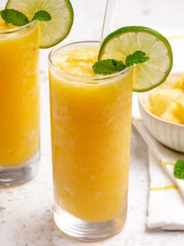Pineapple slushie in a glass with a lime wheel, sprig of mint, and a straw.