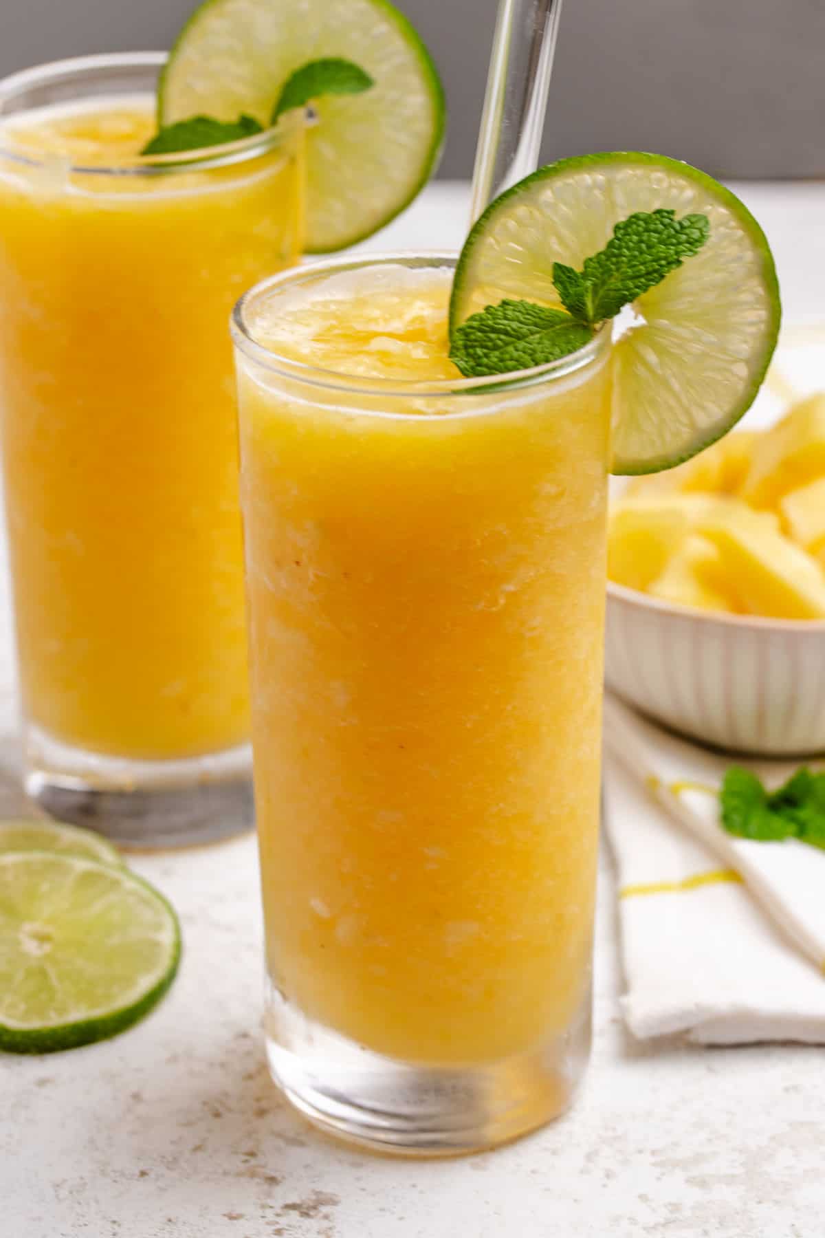 Pineapple slushy in a glass with a lime wheel, mint, and a straw.