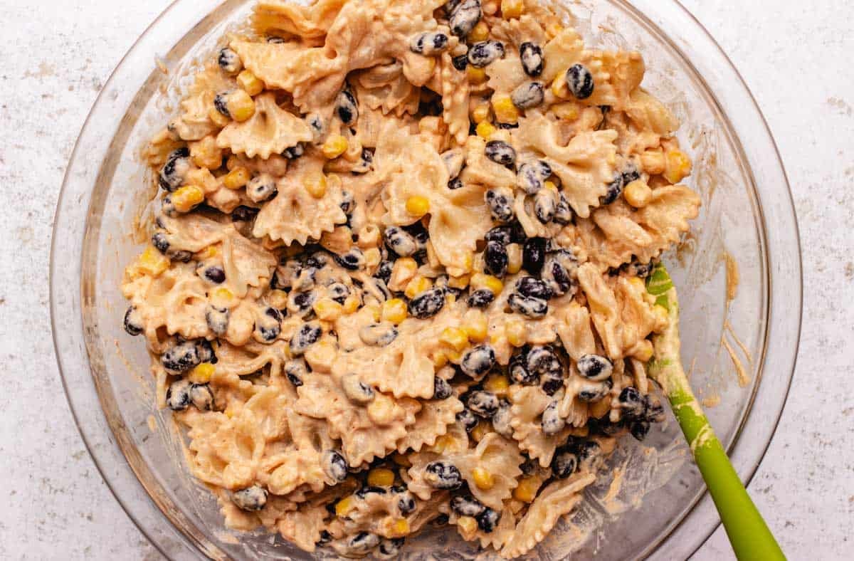 A bowl with cooked pasta, black beans, and corn coated in a vegan southwest dressing for a cold vegan pasta salad.