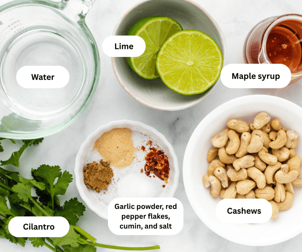 A bowl of water, limes, maple syrup, cilantro, seasonings, and cashews on a table.