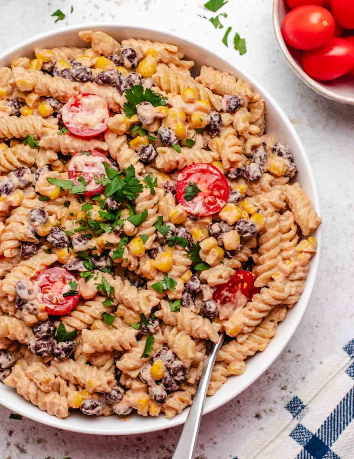 Cold vegan pasta salad with cherry tomatoes, black beans, and corn in a white bowl with a fork.