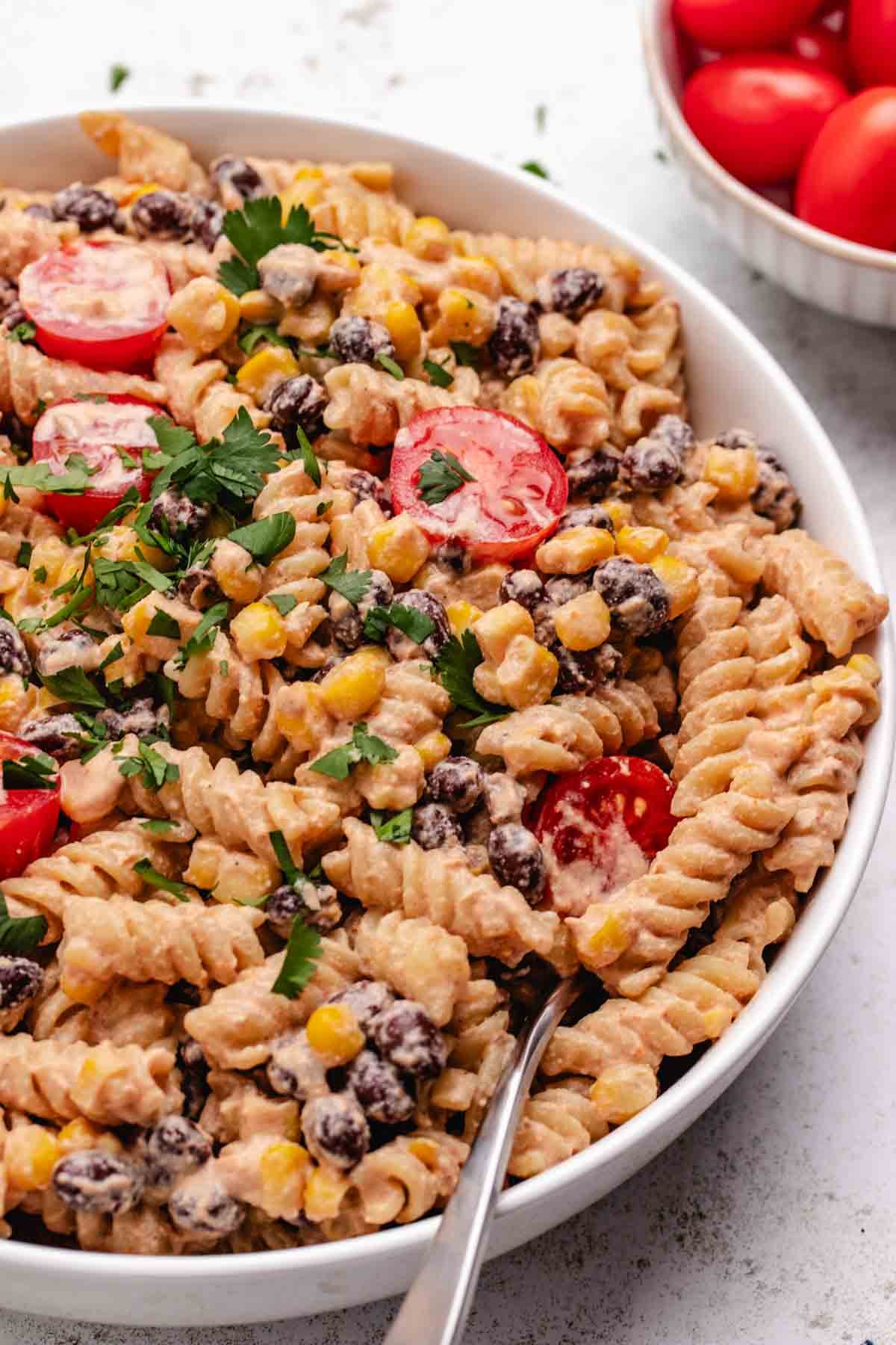 Vegan pasta salad with tomatoes, black beans, and corn in a white bowl with a fork.