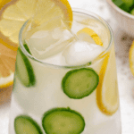 Cucumber lemon ginger water in a glass with sliced cucumber and a lemon slice.