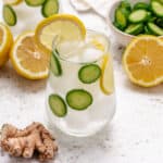Ginger cucumber and lemon water in a glass with sliced cucumbers and a lemon slice.