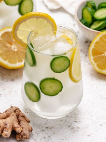Ginger cucumber and lemon water in a glass with sliced cucumbers and a lemon slice.