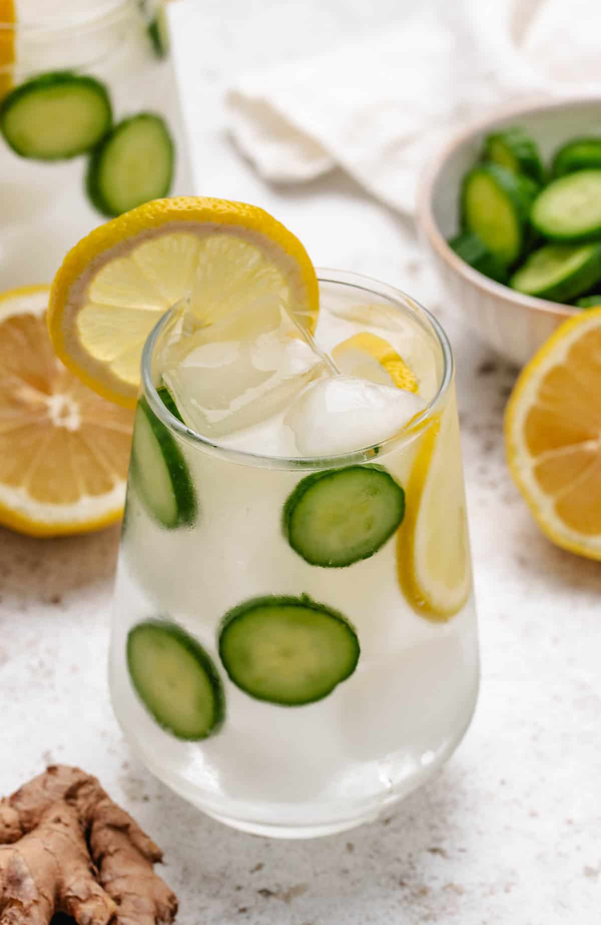 Cucumber lemon ginger water in a glass with sliced cucumber and a lemon slice.
