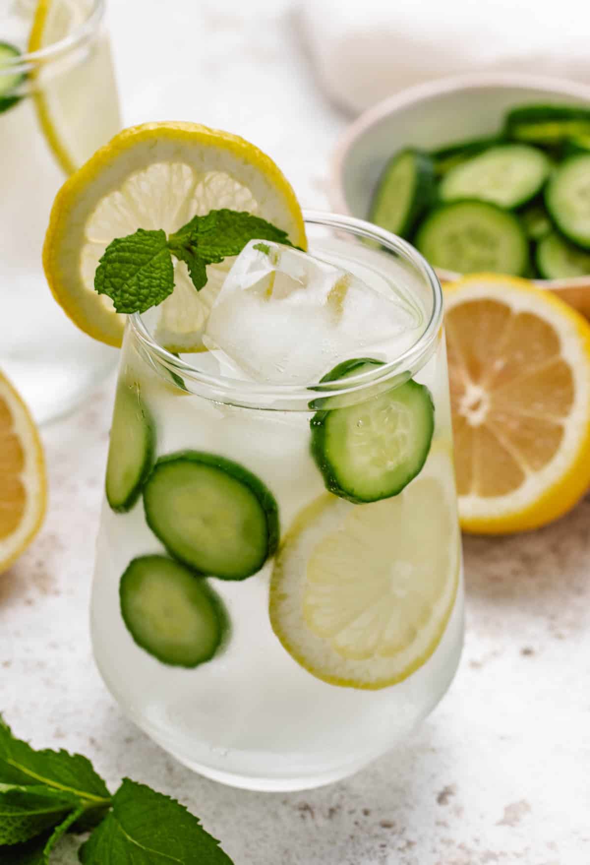 Lemon mint and cucumber water in a glass with a lemon slice and a mint sprig.