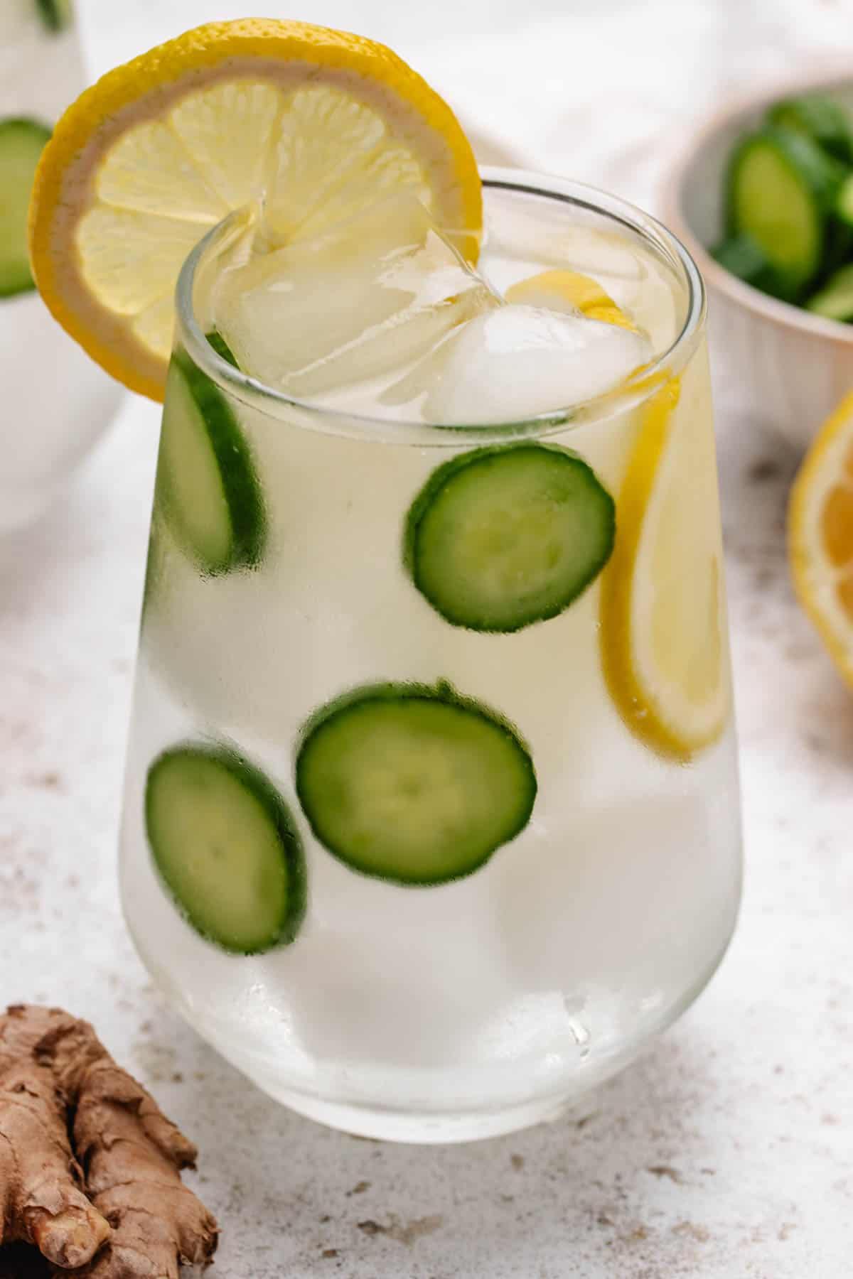 Cucumber lemon ginger water in a glass with sliced cucumber and a lemon slice.