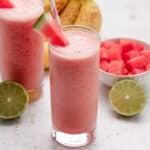 Watermelon banana smoothie in a glass with a slice of watermelon and a straw.