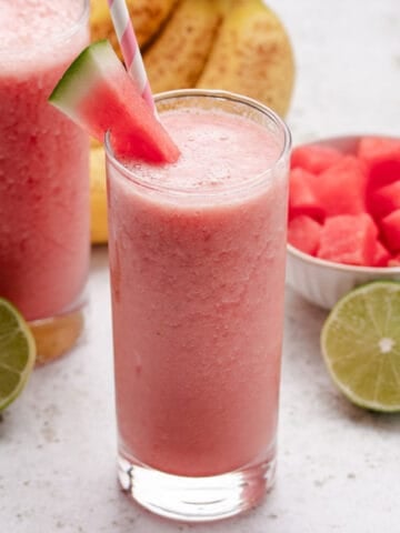 Watermelon banana smoothie in a glass with a slice of watermelon and a straw.