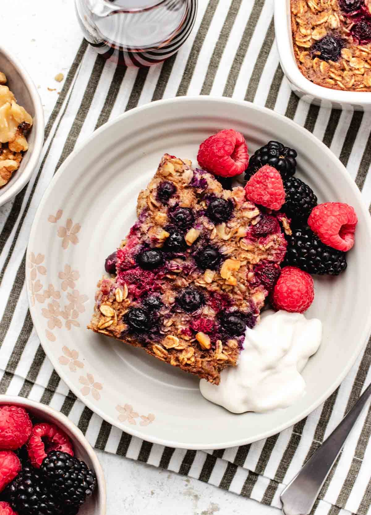 Baked vegan oatmeal on a plate with berries and dairy-free yogurt.