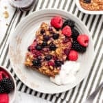 A slice of vegan baked oatmeal on a plate with berries and dairy-free yogurt.