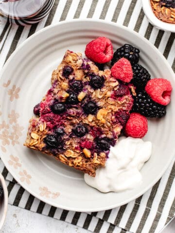 A slice of vegan baked oatmeal on a plate with berries and dairy-free yogurt.