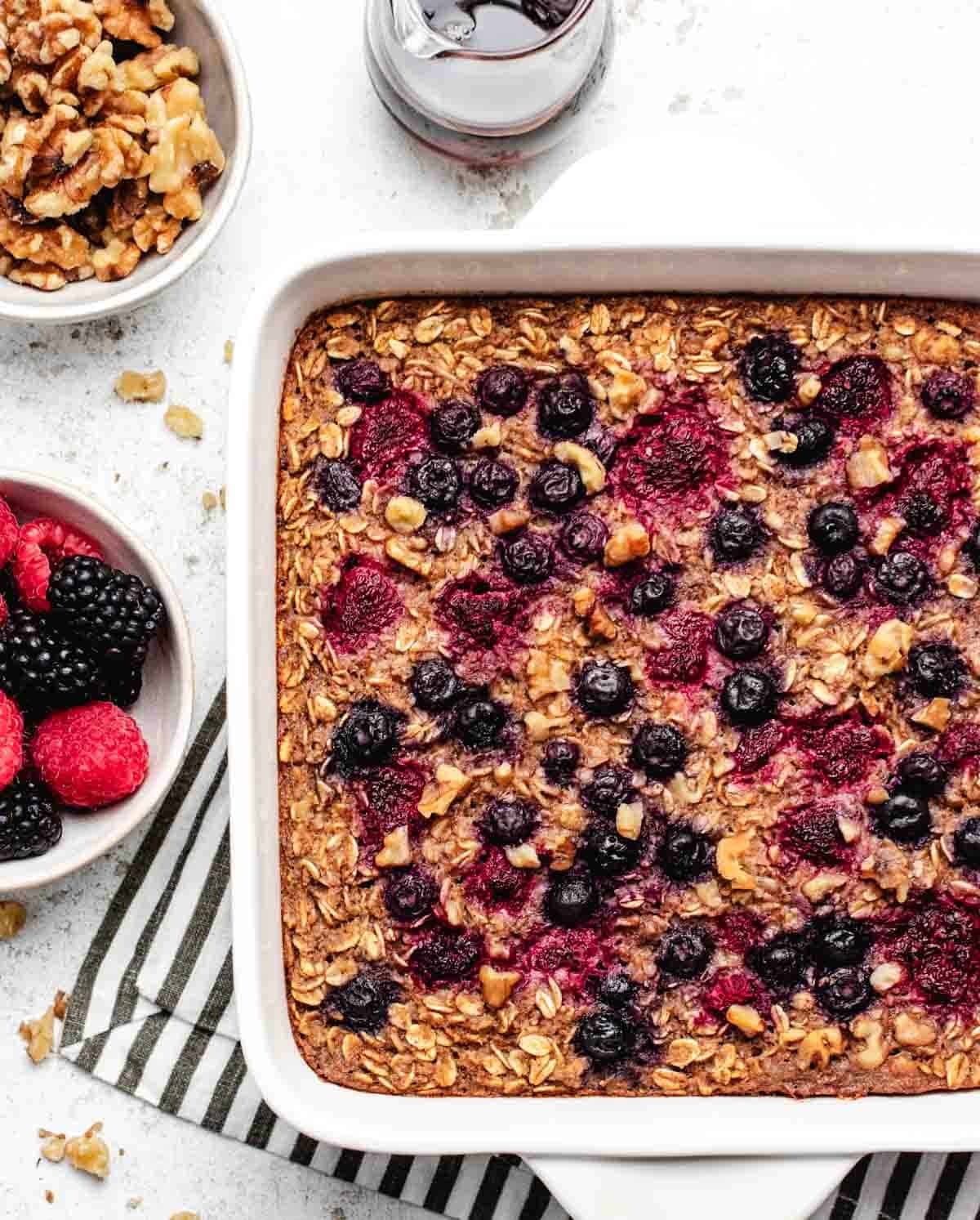 Healthy vegan baked oatmeal with frozen berries in a baking dish with a bowl of berries.
