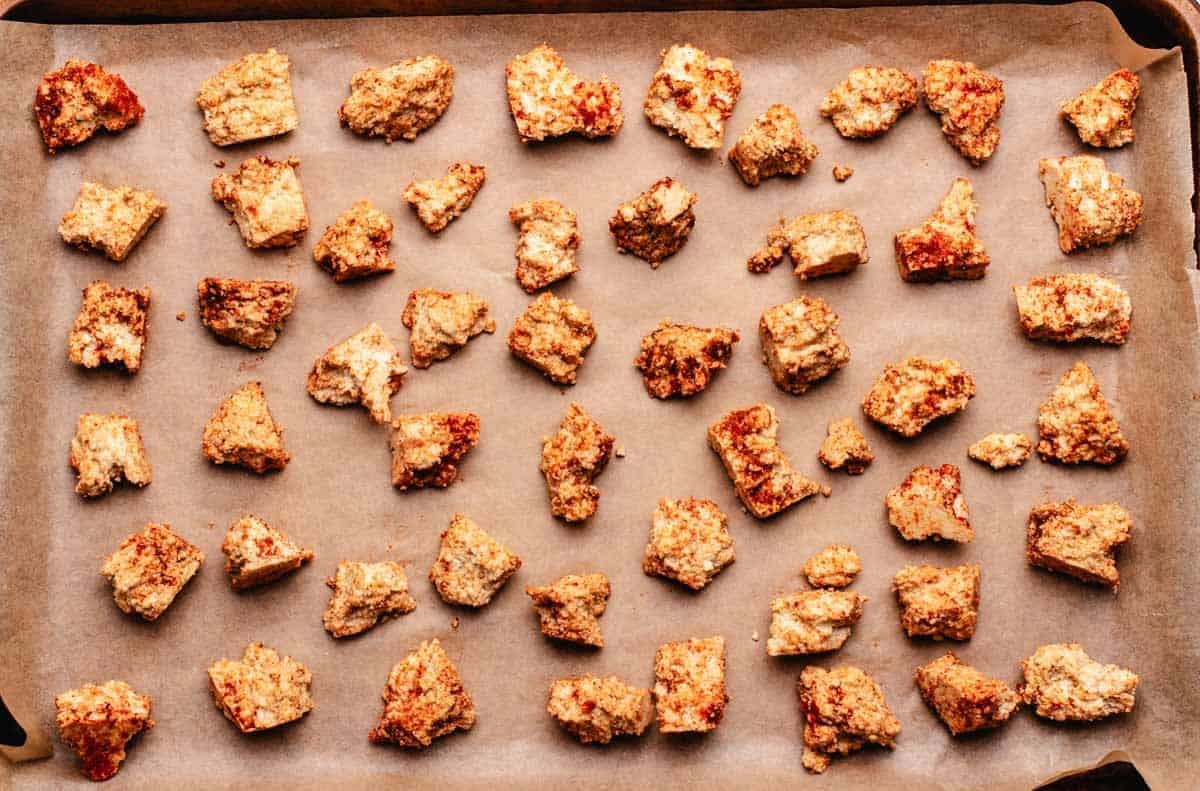 Tofu pieces coated in spices on a baking tray with parchment paper.