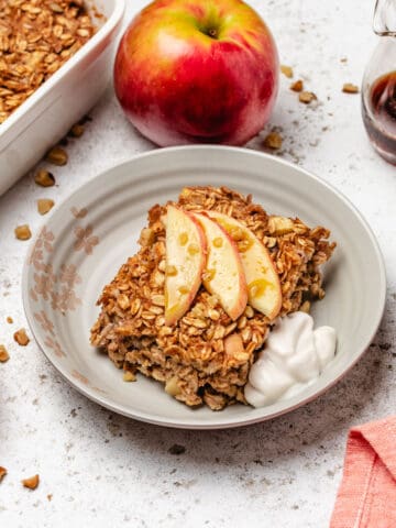 Vegan baked oatmeal with apples on a plate with dairy-free yogurt and sliced apples.