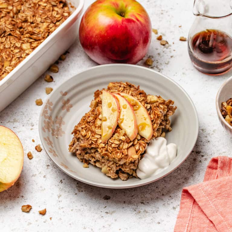 Vegan apple baked oatmeal on a plate with dairy-free yogurt and sliced apples.