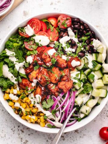 BBQ tofu salad with corn, cherry tomatoes, lettuce, red onions, cucumbers, black beans, and vegan ranch dressing in a bowl with a fork.