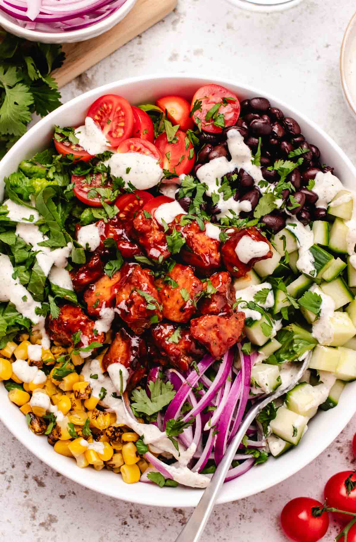 Vegan tofu salad with BBQ tofu, cucumber, corn, red onions, lettuce, cherry tomatoes, black beans, and vegan ranch dressing in a bowl with a fork.