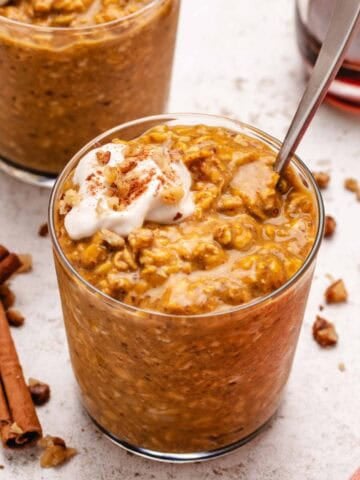 Pumpkin overnight oats in a glass jar with dairy-free yogurt and walnuts on top.
