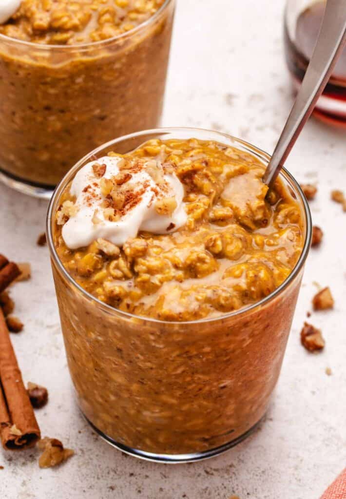 Pumpkin overnight oats in a glass jar with dairy-free yogurt and walnuts on top.