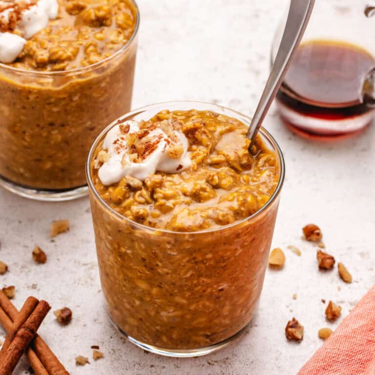 Vegan pumpkin overnight oats in a glass jar with dairy-free yogurt and walnuts on top.